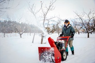 Caucasian man using snow blower in snowy field
