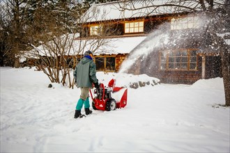 Caucasian man using snow blower in snowy driveway
