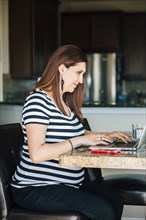 Pregnant Hispanic woman using laptop in kitchen