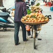 Vendor pushing bicycle with fruit for sale