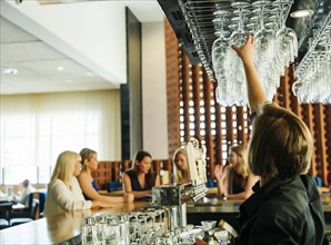 Caucasian bartender reaching for wine glass at bar