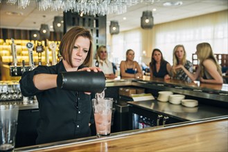 Caucasian bartender pouring cocktail from mixer into glass