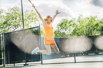 Caucasian woman jumping for joy on tennis court
