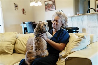 Black woman sitting on sofa playing with dog