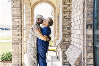Black soldier kissing wife on front stoop