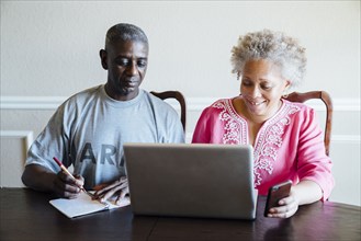 Black couple using laptop and cell phone at table