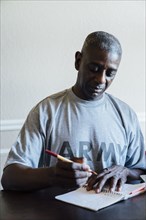 Black man writing in notebook at table