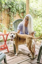 Caucasian woman holding cell phone petting dog on backyard patio