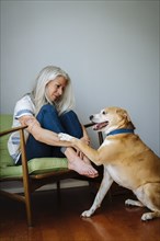 Caucasian woman sitting in armchair playing with dog
