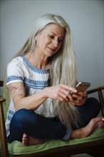 Caucasian woman sitting in armchair texting with cell phone