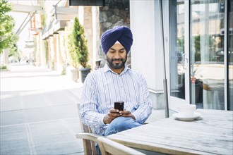 Man wearing turban texting on cell phone at cafe