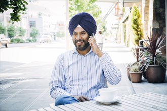 Man wearing turban talking on cell phone at cafe