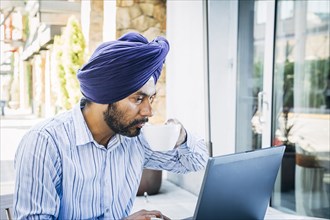 Man wearing turban using laptop at cafe