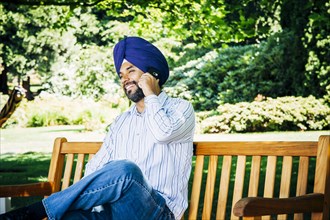 Man wearing turban sitting on park bench talking on cell phone