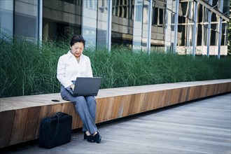 Businesswoman sitting on bench using laptop