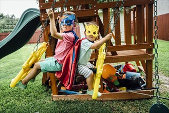 Caucasian brothers wearing superhero costumes on swing