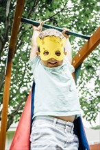 Caucasian boy wearing superhero costume hanging on monkey bars