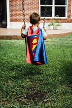 Caucasian boy wearing superhero costume on swing