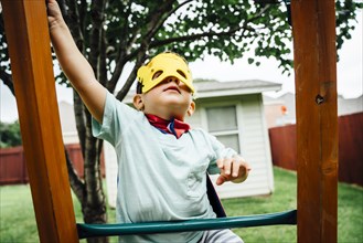 Caucasian boy wearing superhero costume climbing on backyard playground