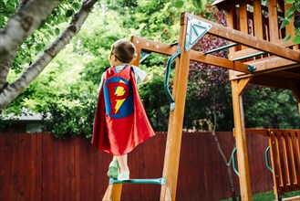 Caucasian boy wearing superhero costume climbing on backyard playground