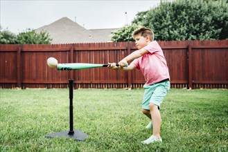 Caucasian boy hitting baseball off tee in backyard