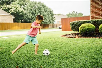 Caucasian boy kicking soccer ball on lawn