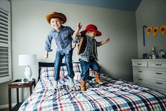 Caucasian boys wearing cowboy costumes jumping on bed