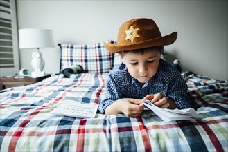 Caucasian boy wearing cowboy costume reading booklet on bed