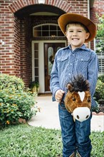 Caucasian boy wearing cowboy costume riding toy horse