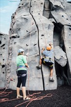 Woman holding rope for man climbing rock climbing wall