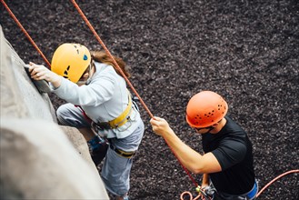 Caucasian man holding rope for woman climbing rock climbing wall