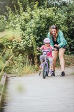 Mother watching daughter riding bicycle with training wheels