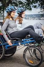 Caucasian mother and daughter riding tandem bicycle