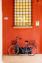 Blue bicycle leaning on orange wall under window