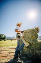Caucasian farmer lifting bale of hay
