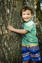 Portrait of smiling Caucasian boy hugging tree