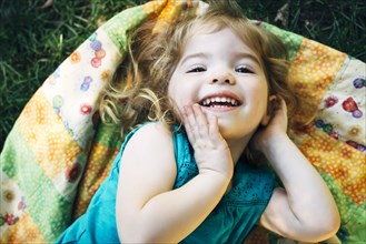 Portrait of smiling Caucasian preschool girl laying on blanket outdoors