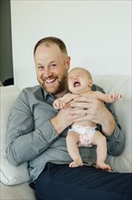 Portrait of smiling father holding crying baby daughter