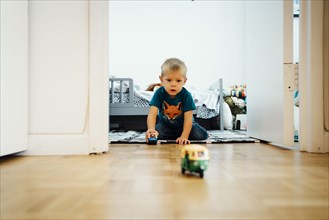 Boy kneeling on floor pushing toy cars