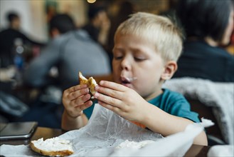 Mixed Race boy eating messy bagel in restaurant