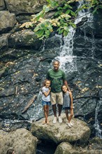Father and daughters posing on rock near waterfall
