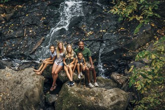 Multi-ethnic family posing on rock near waterfall