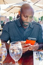 Black man sitting at restaurant table texting on cell phone