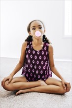 Mixed Race girl sitting on floor blowing bubble with gum