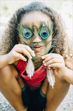 Mixed Race girl covering eyes with peacock feathers