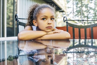Pensive Mixed Race girl leaning on glass table