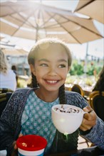 Smiling Mixed Race girl drinking from cup in restaurant