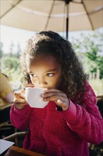 Mixed Race girl sipping from cup in restaurant