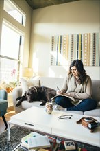 Mixed Race woman on sofa with dog writing in journal