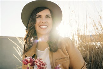 Portrait of smiling Mixed Race woman wearing hat holding flowers